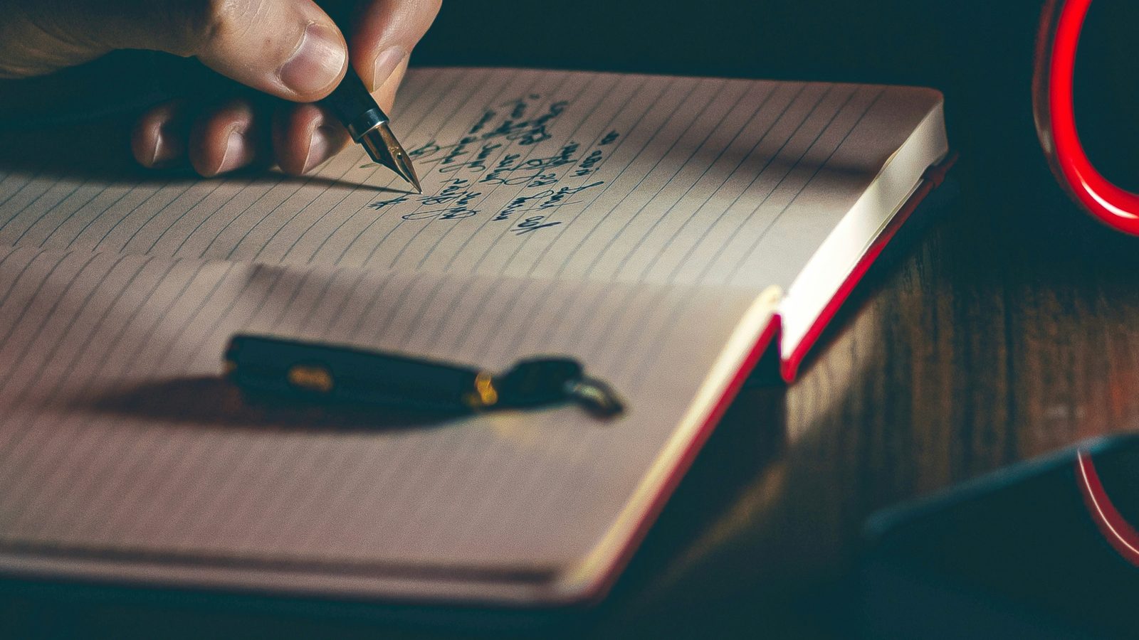 A hand writing in a notebook with a fountain pen, low light